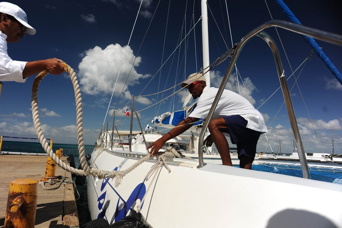 Dos tripulantes asegurando las amarras de un velero en un muelle del Caribe bajo cielo despejado