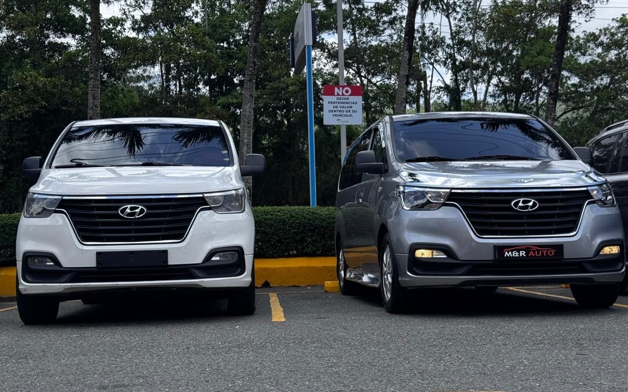 Dos minivans Hyundai H1, una blanca y una gris, estacionadas antes de un traslado desde el aeropuerto